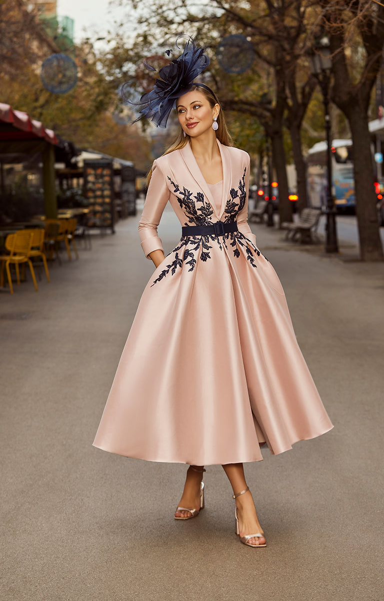 Woman in a pink dress by Veni Infantino  (item number 992541) with black floral patterns standing on a street.