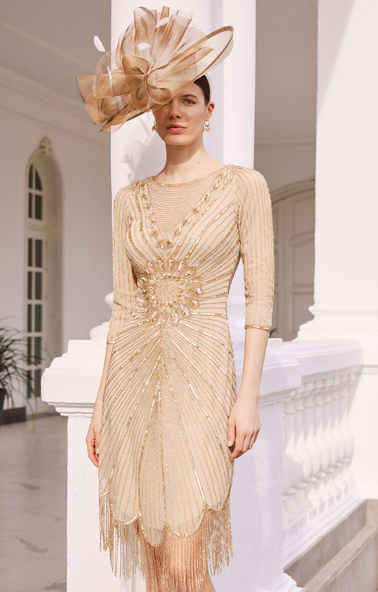 Woman wearing Couture Club by Rosa Clara 1GH8 - Gold Beaded Short Dress with 3/4 Sleeves with a large bow headpiece in an elegant setting.