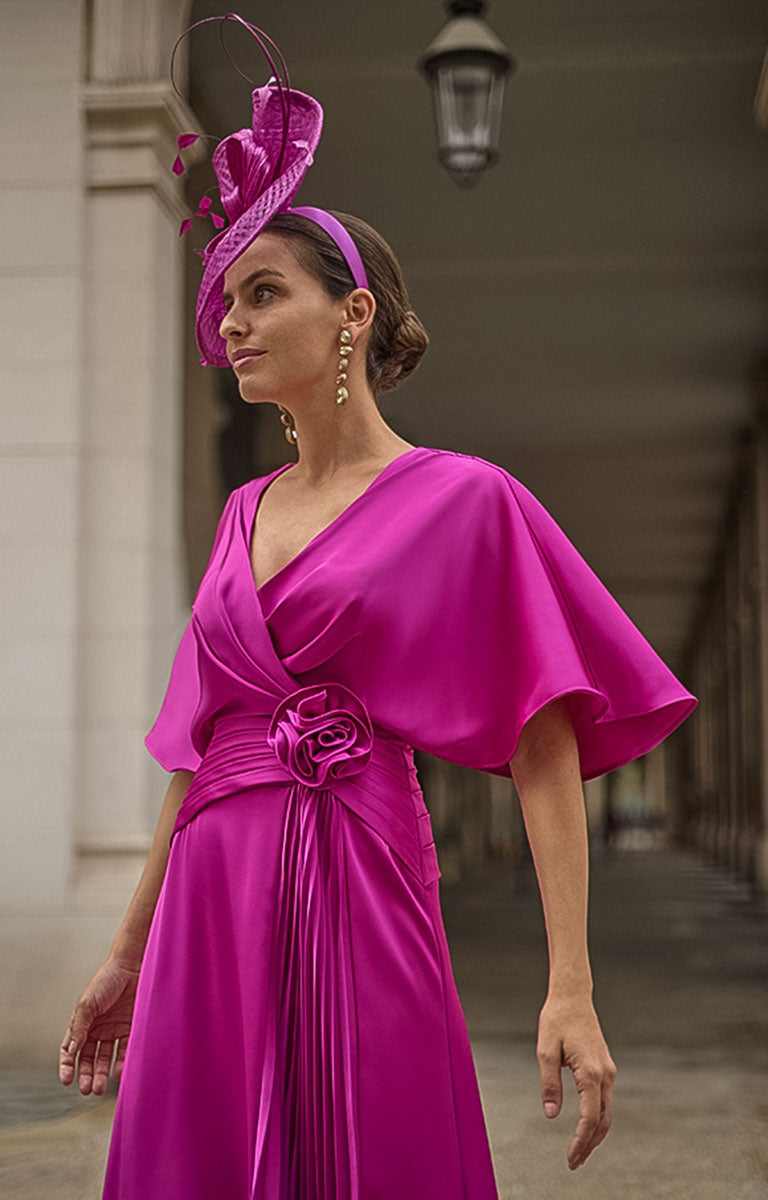 Woman in Couture Club 2G08 - Geranium Satin Occasion Dress with Contemporary Elegant Styling with matching headpiece standing outdoors.