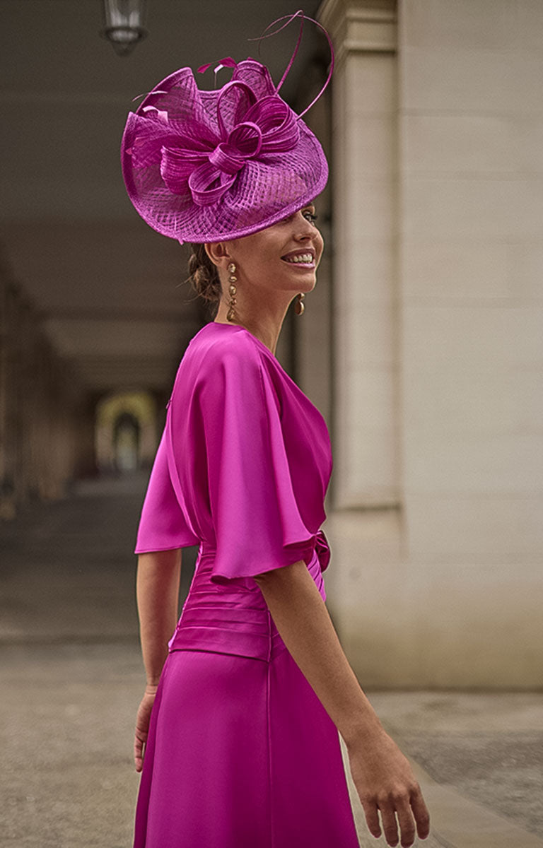 Woman wearing Couture Club 2G08 - Geranium Satin Occasion Dress with Contemporary Elegant Styling and matching hat in an outdoor setting