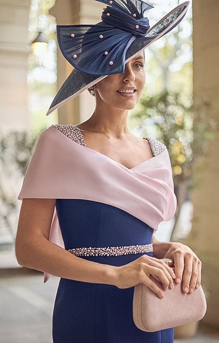 Close up photograph of Woman wearing Couture Club 2G13 - Navy and Pale Rose Crepe Midi Dress with Elegant Colour-Block Design against an elegant courtyard background  with potted olive trees.