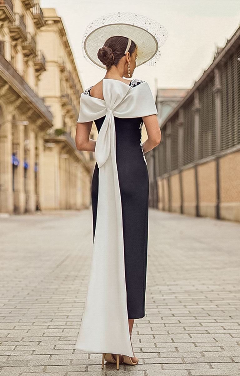 Woman in a Couture Club 2G14 - Black &amp; Natural Crepe Occasion Dress with Elegant Tailored Silhouette with a large bow standing on a street.