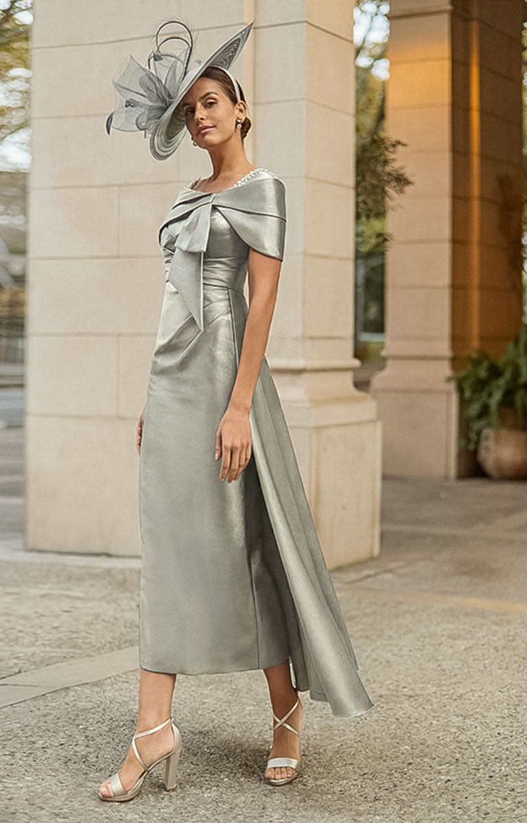 Woman in Couture Club 2G16 - Silver Mika Occasion Dress with Contemporary Elegant Styling with a large bow and matching hat standing outdoors.