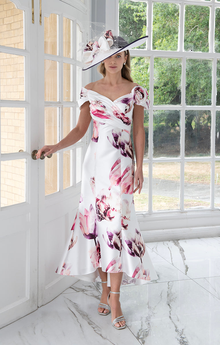 Woman in Irresistible IR8806G - Pink and Fuchsia Fit-and-Flare Midi Dress with Off-Shoulder Neckline standing in a bright room with large windows.