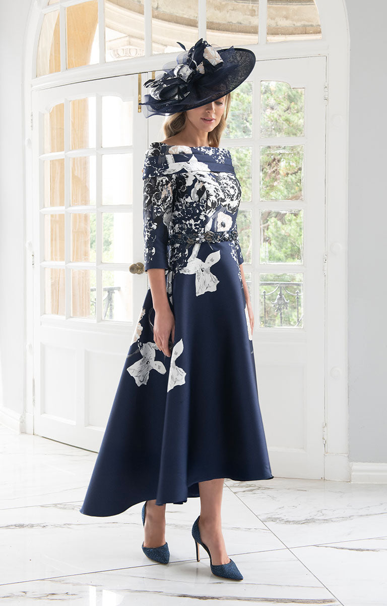 Woman wearing Irresistible IR8832TJ - Navy Print Midi Dress with Off-Shoulder Design with white floral patterns and a matching hat indoors.