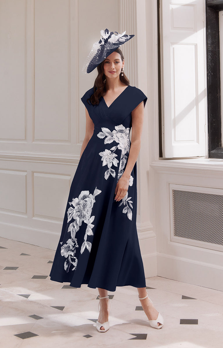Lady wearing John Charles 66718 - Navy &amp; Ivory A-Line Midi Dress with Embroidered Detail standing in an elegant room with marble floor.