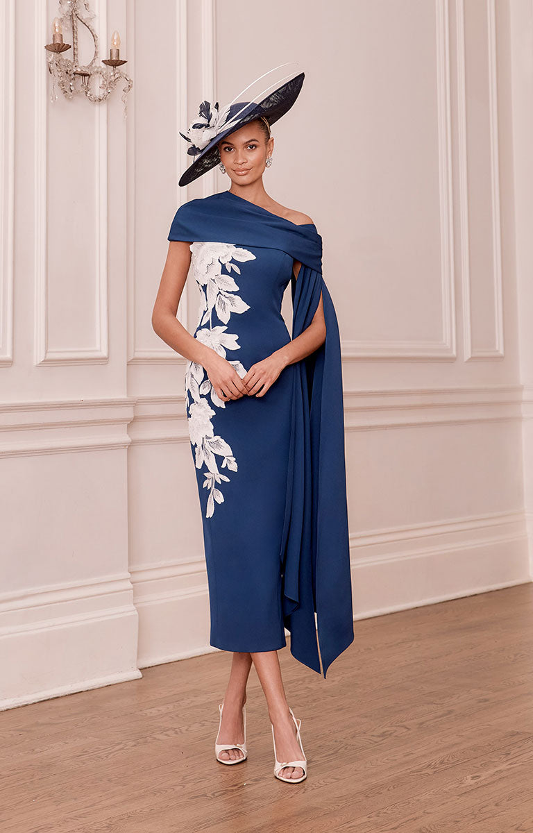 Woman wearing John Charles 66790 - Navy and Ivory Crepe Midi Dress with Detachable Cape and a matching hat indoors.