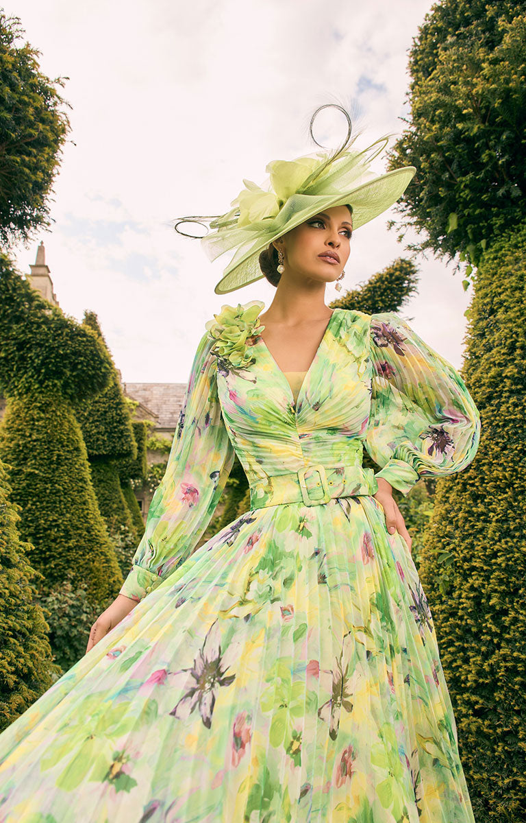 Woman wearing Veni Infantino 992770 - Lime / Multi A-Line Satin Dress with 3D Ruffle Shoulder complimented with a large hat standing in a garden path with greenery around.