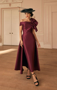 Woman in Veni Infantino 992820 - Maroon Occasion Dress with Elegant Contemporary Styling with a large bow, standing in an elegant room.