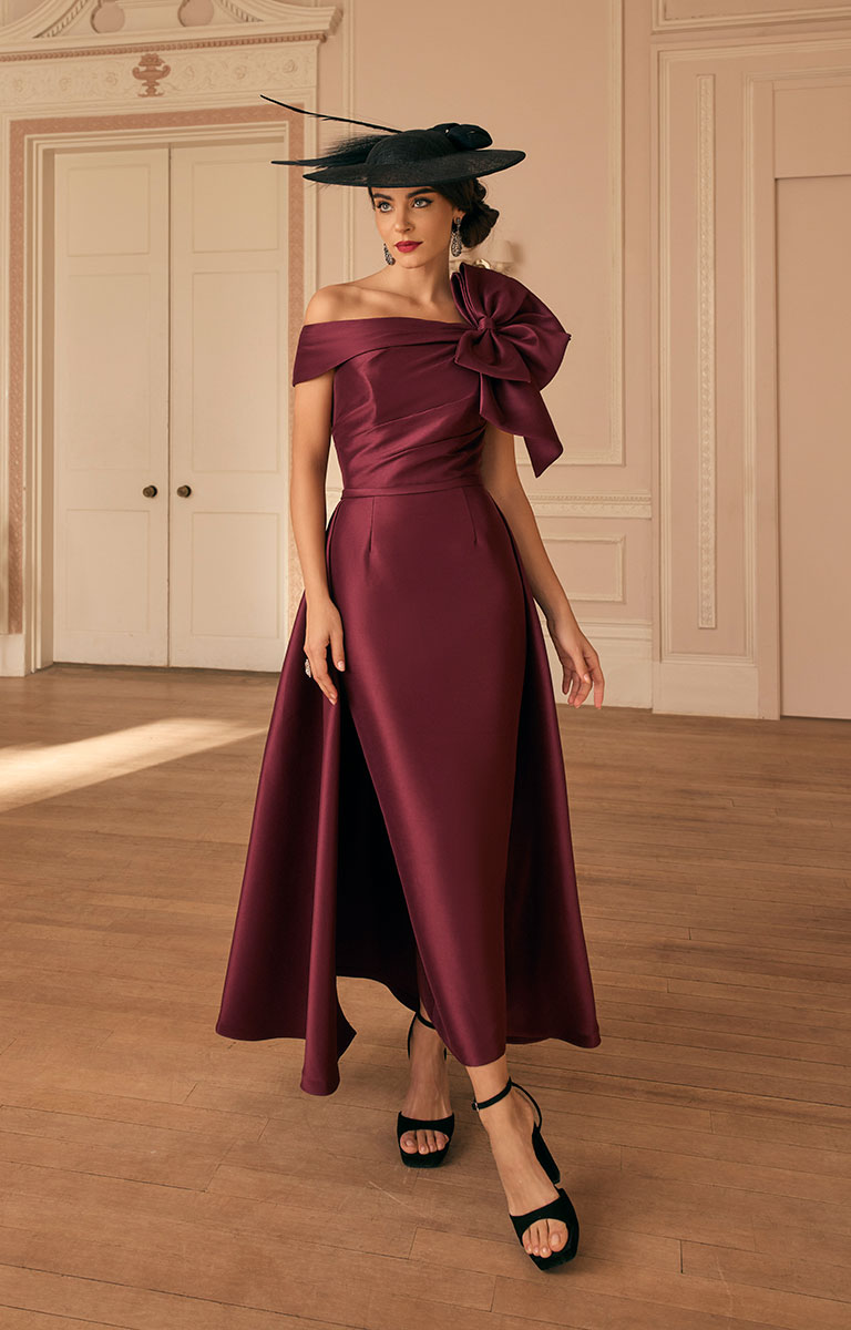 Woman in Veni Infantino 992820 - Maroon Occasion Dress with Elegant Contemporary Styling with a large bow, standing in an elegant room.