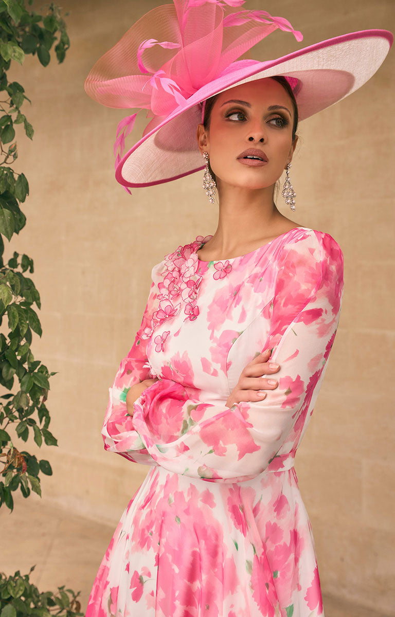 Woman in Veni Infantino 992775 - Cherry Blossom Ankle-Length Chiffon Dress with Bateau Neckline and 3D Floral Detail on one-shoulder with a matching hat standing in front of a building.