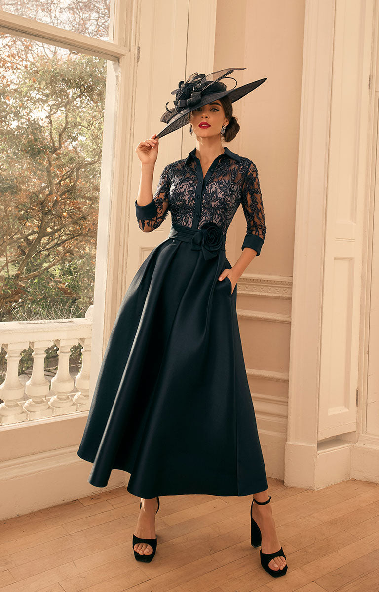 Woman in Veni Infantino 992805 - French Navy Occasion Dress with Silver Embroidery and a matching hat standing in a room with large windows.